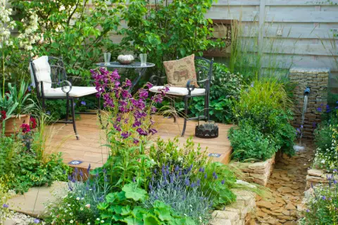 Gemütliche Sitzecke mit Gartenmöbeln und Pflanzen in einem blühenden Garten.