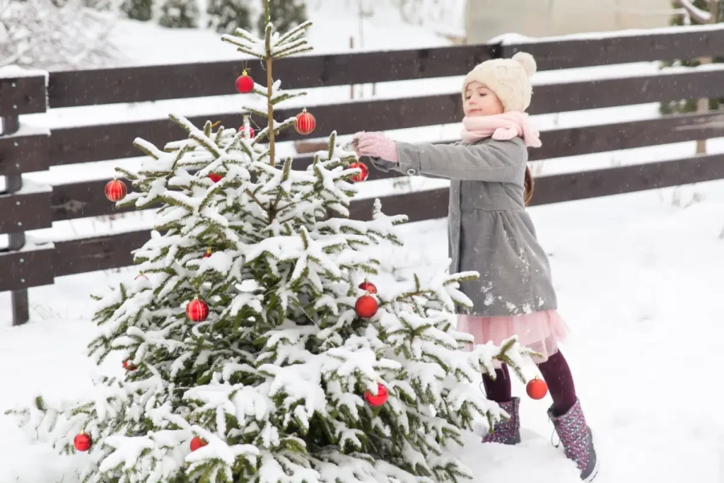Mädchen schmückt Weihnachtsbaum im Garten mit Weihnachtskugeln.