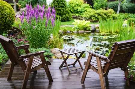 Zwei Stühle stehen neben dem Gartenteich.
