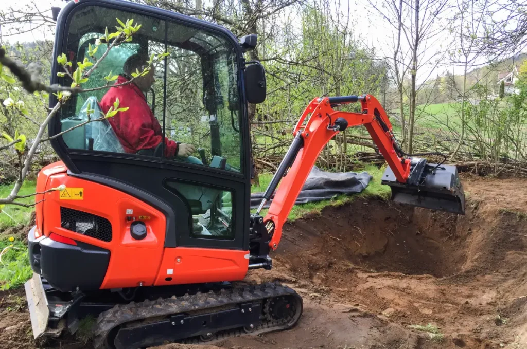 Mann hebt mit kleinem Bagger eine Grube für den Gartenteich aus.