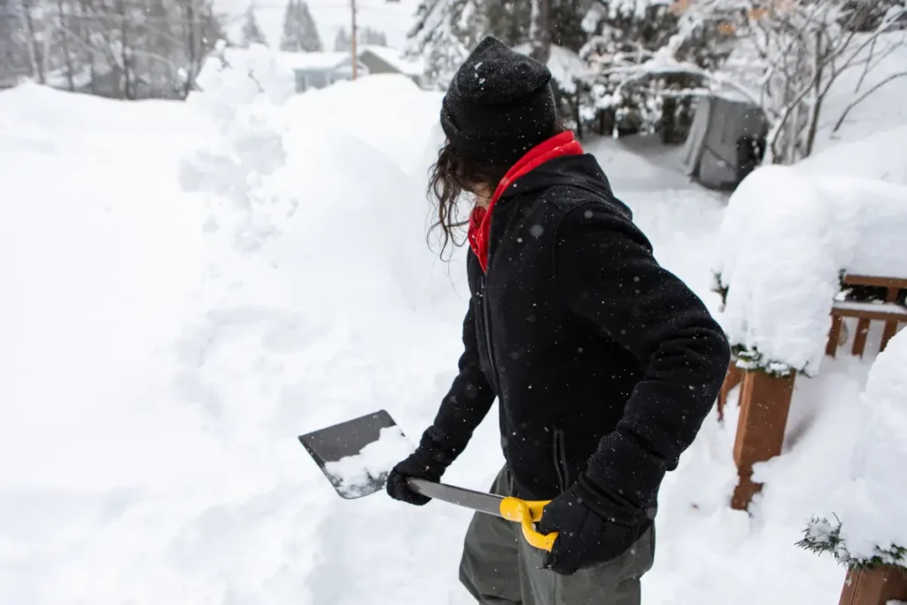 Person schippt Schnee mit Schneeschippe.