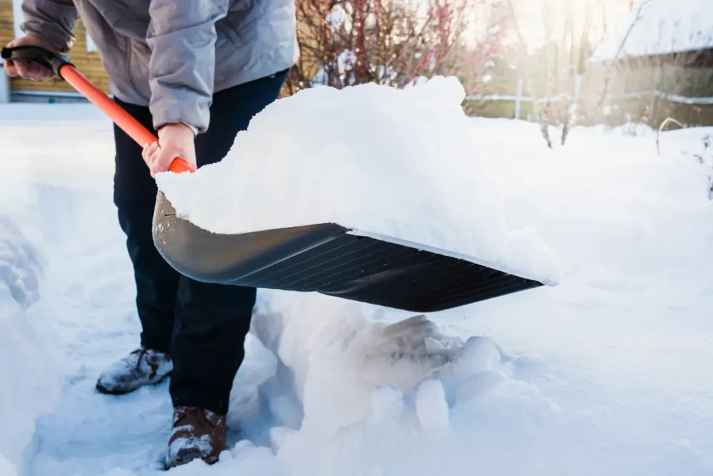 Eine Person schaufelt Schnee mit der Schneeschaufel.