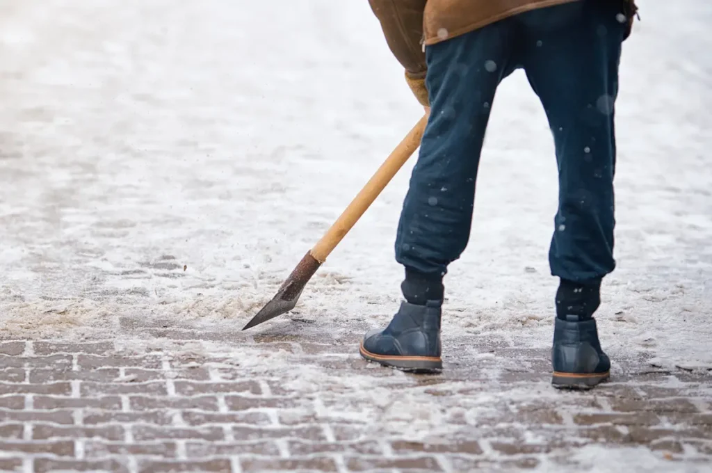 Eine Person löst mit einem Eisstößer verkrusteten Schnee vom Gehweg.