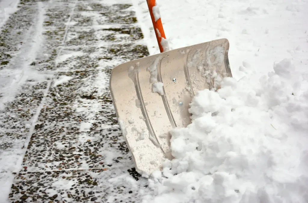 Person schiebt Gehweg mit Schneeschieber frei.