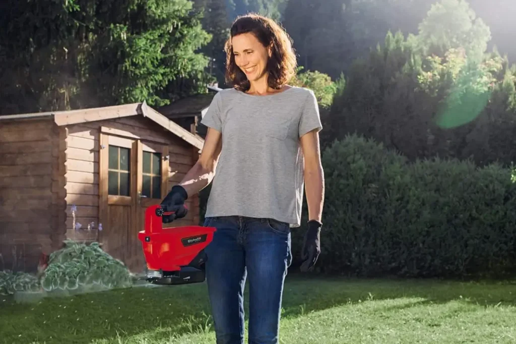 Frau streut im Garten mit Streuer Rasensamen aus.