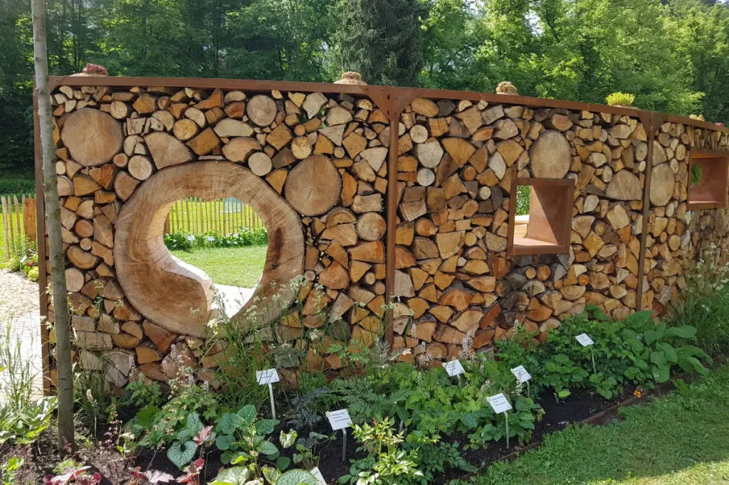 Brennholz zu einer Wand an der Terrasse im Brennholzregal gestapelt, mit Gucklöchern in Form eines Herzens und einem Fenster.