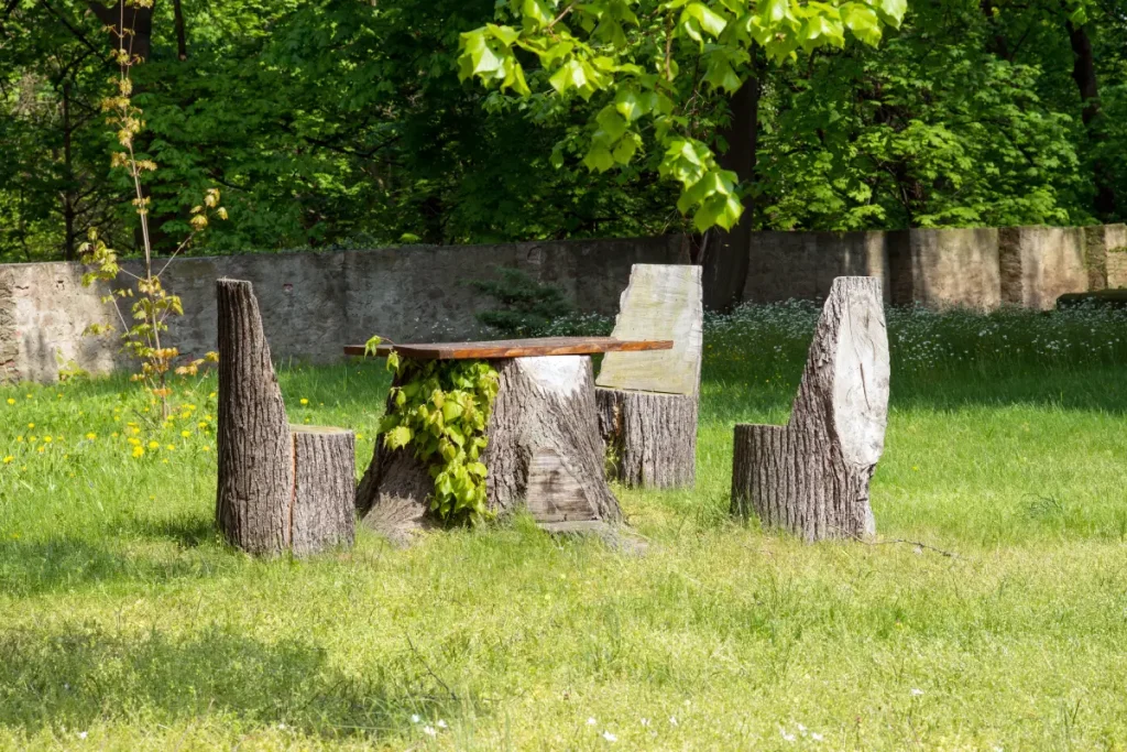 Aus Baumstämmen gesägte Sitzgruppe mit drei Sesseln und eim Tisch im Garten.