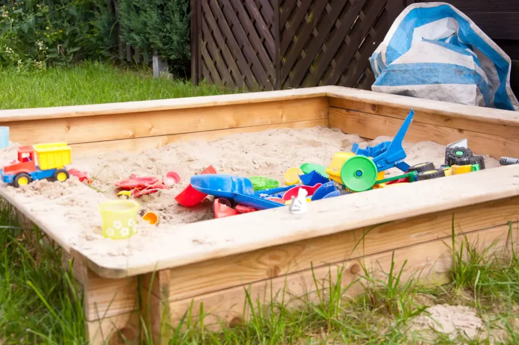 Schlichter Sandkasten aus vorgefertigtem Holzrahmen mit Spielzeug im Sand.