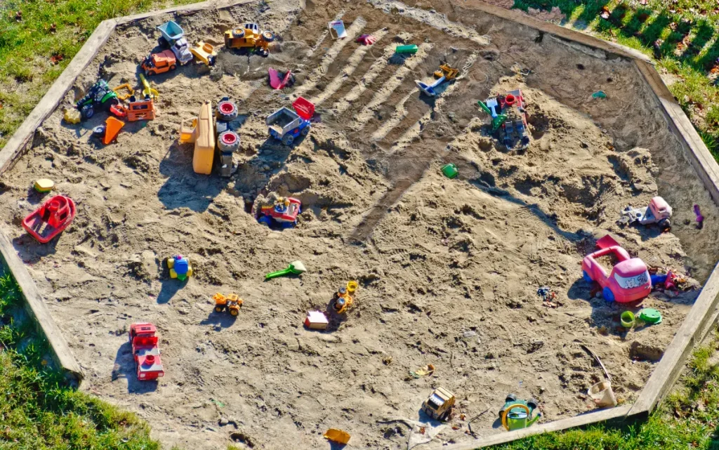 Sandkasten mit Holzumrandung, gefüllt mit viel Sandspielzeug.