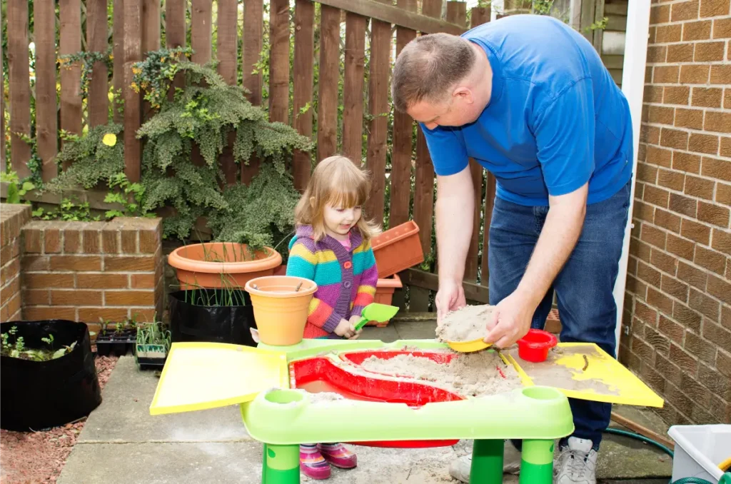 Vater und Tochter stehen am Sandkastentisch.