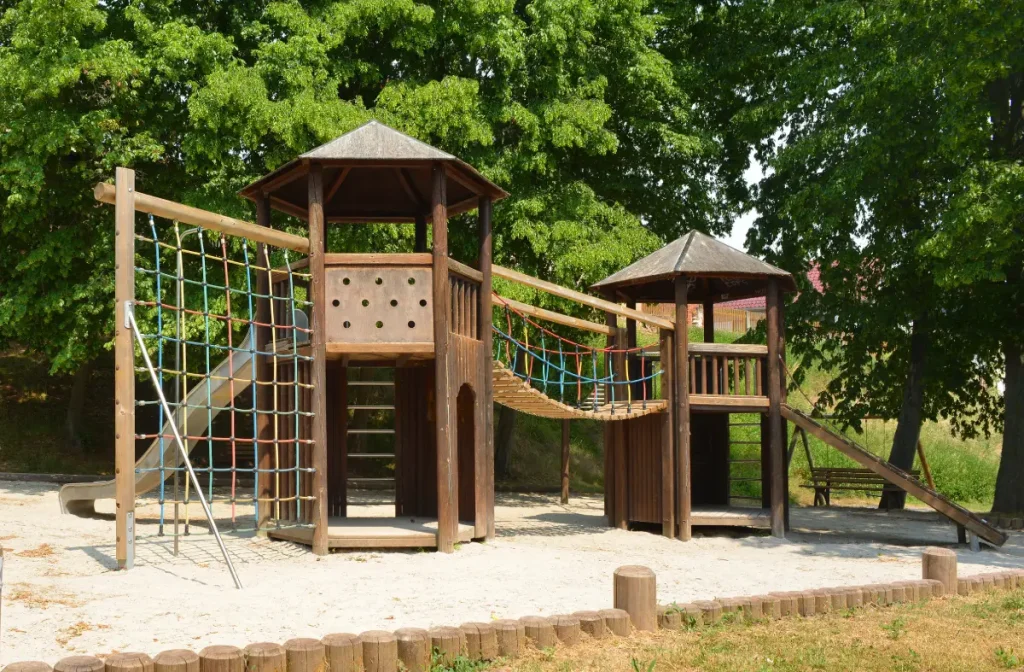 Spielplatz mit Kletterturm und Rutsche steht im großen Sandbett.