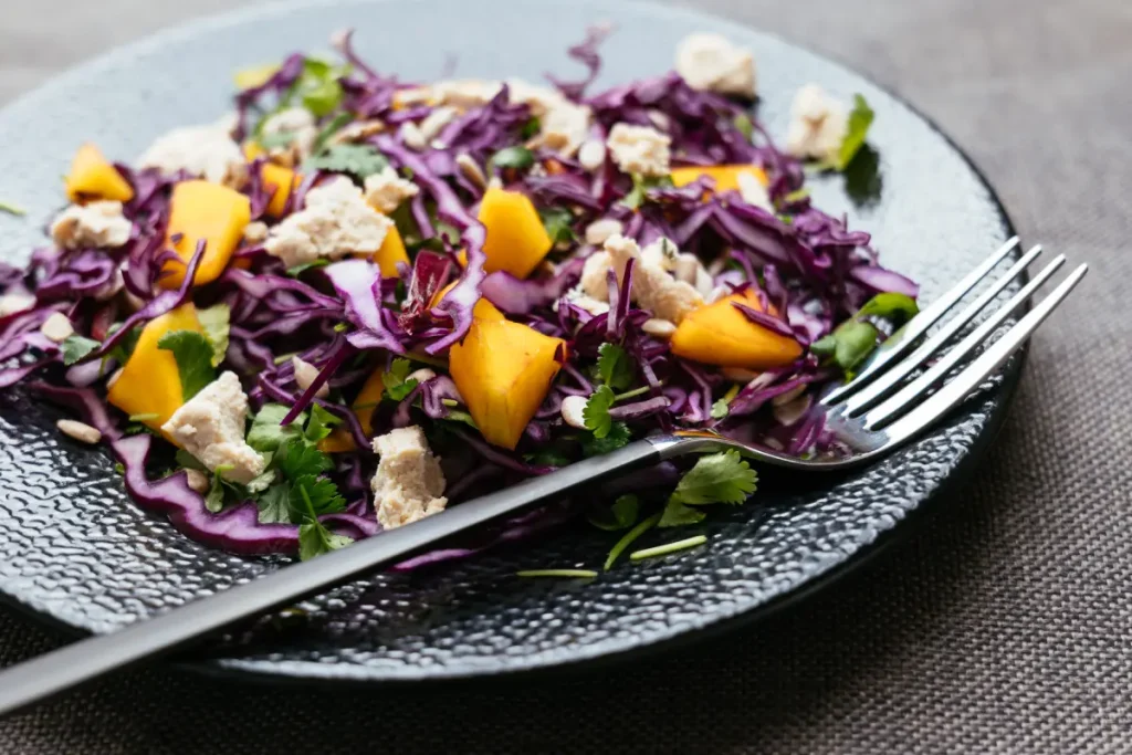 Frischer roher Rotkohl mit Mango und Feta auf einem Teller.